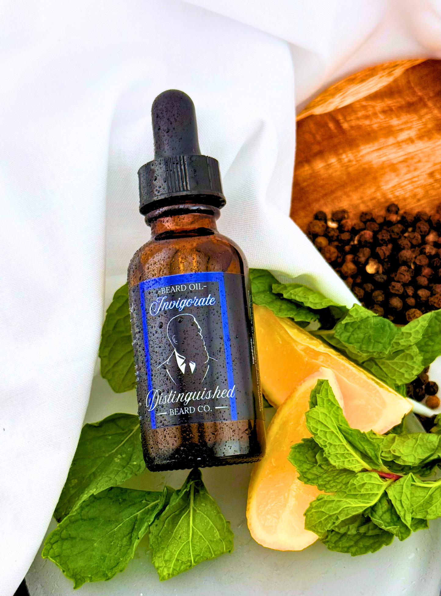 Bottle of 'Invigorate' with a dropper on a white surface with green leaves and a lemon.