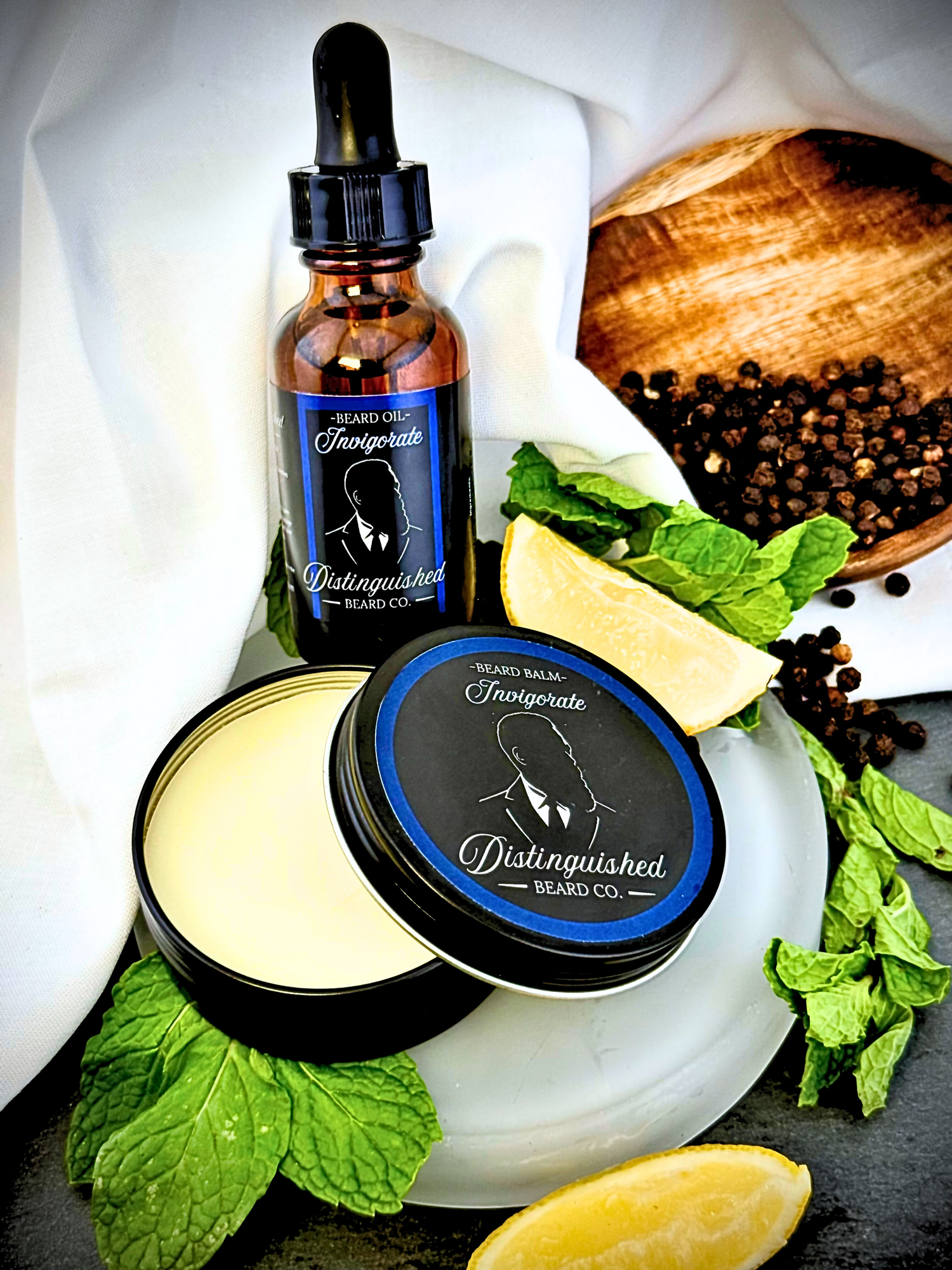 Beard care products including a bottle, jar, and leaves on a white cloth with a wooden bowl in the background.